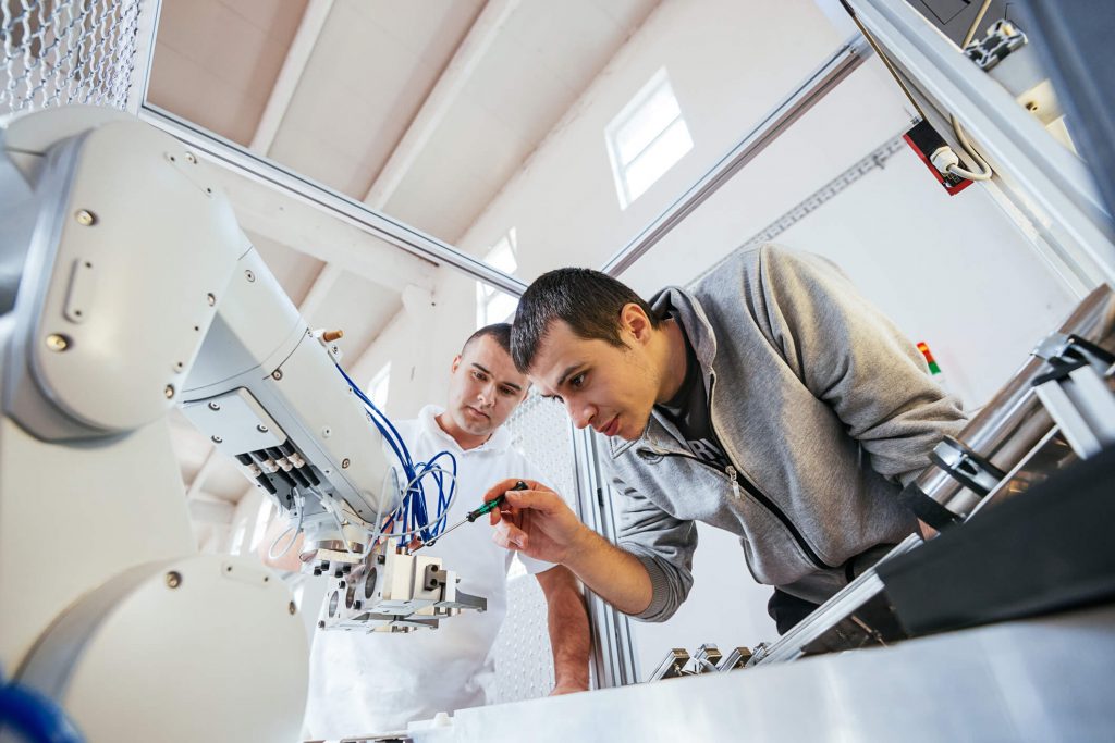 Técnicos ajustando braço robótico em laboratório, ilustrando BPO e RPA na robótica
