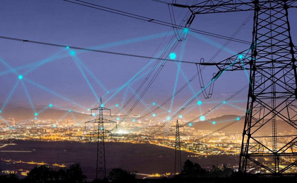 Torre de transmissão de energia com conexões digitais sobre cidade iluminada à noite, representando smart grids